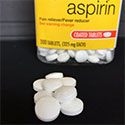 Several aspirin tablets appear on table in front of bottle of aspirin medications