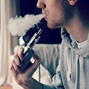 Photo of young man vaping, exhaling cloud of smoke.