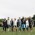 Diverse group of adults and older adults walking hand-in-hand through an open field.