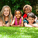 Four children of different ethnicities pose for photo laying on the grass facing the camera.