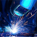 Welder in the process of welding metal, with sparks emanating from tools.