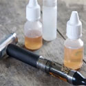 Vaping device and two vials of vaping substance displayed on table.